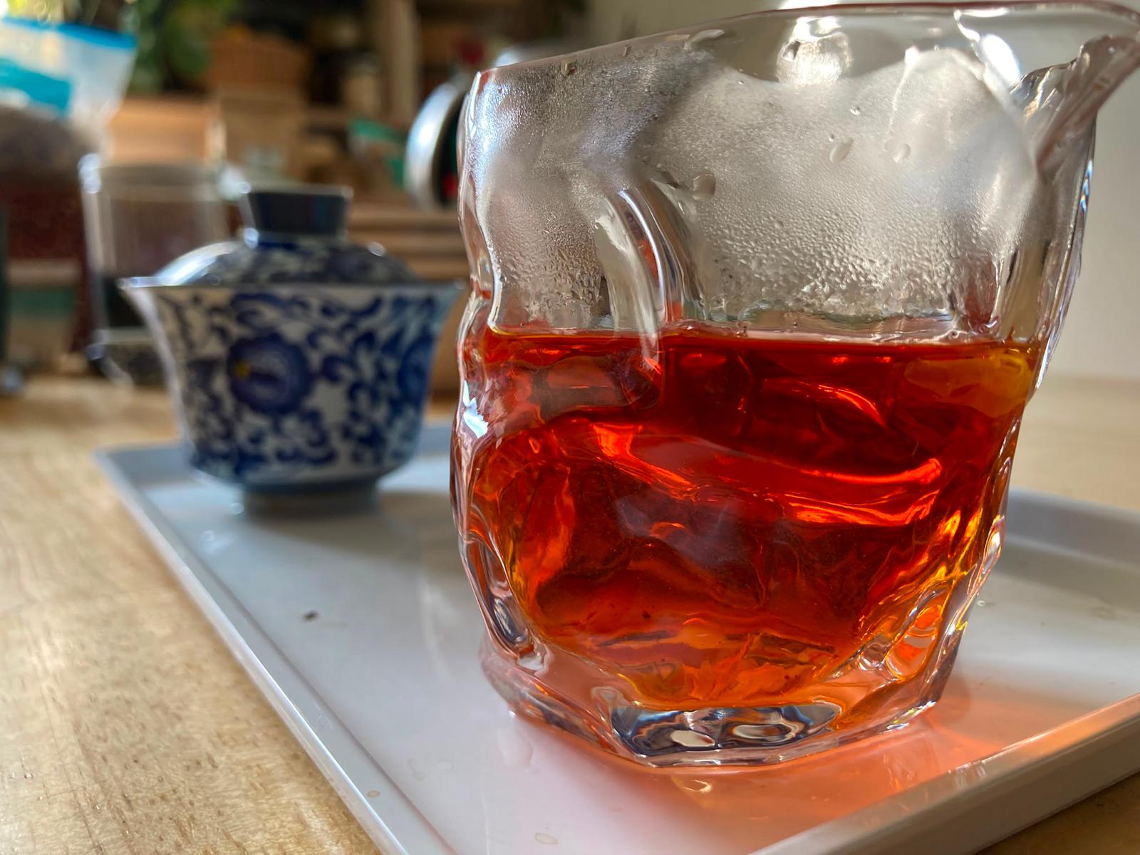 Bingdao golden brick brewed, deep red liquor in a glass pitcher beside a gaiwan