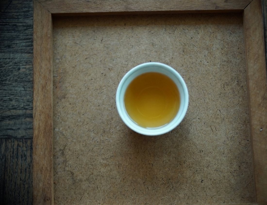 Golden liquor of 1990 Dayuling in a white cup on a wooden tray