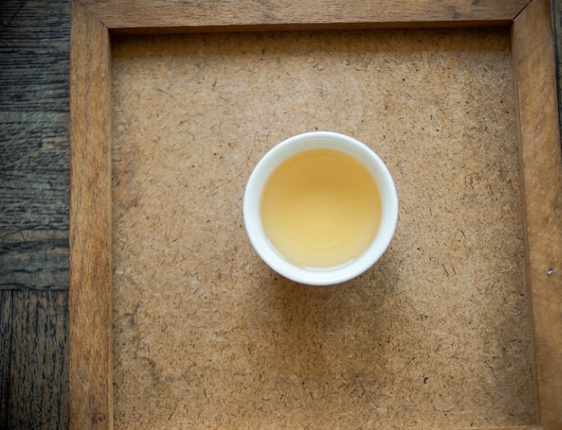 Pale golden Dong Ding liquor in a white cup on a wooden tray