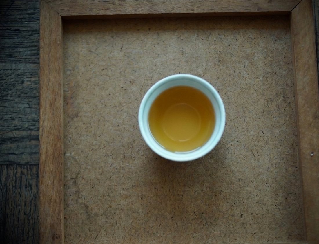 Pale golden Shui Yuan Tou liquor in a white cup on a wooden tray