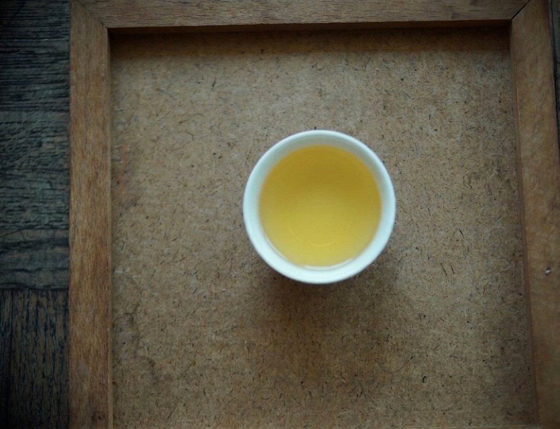 Pale golden Tian Chi liquor in a white cup on a wooden tray