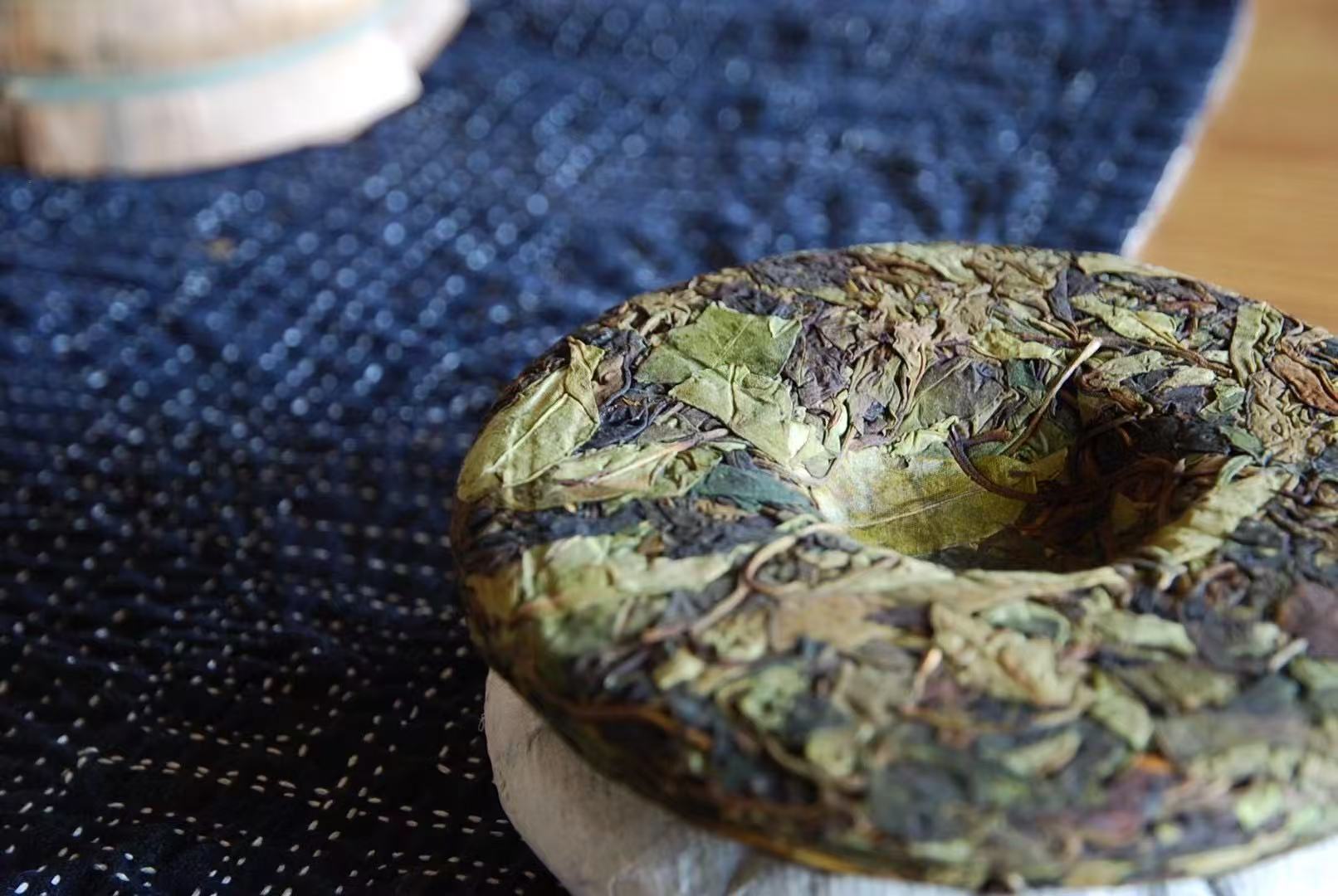 Wild white pu'erh cake close-up, pale pressed leaves on indigo cloth